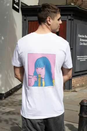 Kanada-Ya | Ramen Near Me | A person wearing the Noodle Girl Ni T-shirt, featuring a girl with blue hair eating noodles on a pink background, stands on a sunny street with buildings behind them. | London