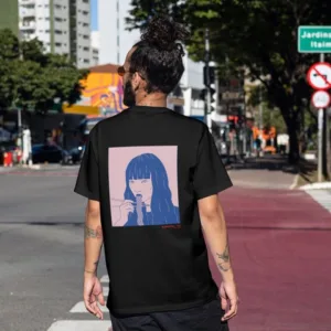 Kanada-Ya | Ramen Near Me | A person with a bun hairstyle is wearing a black Noodle girl Mittsu T-shirt featuring a stylized illustration of a long-haired anime character. Theyre standing on a city street with buildings and trees in the background. | London