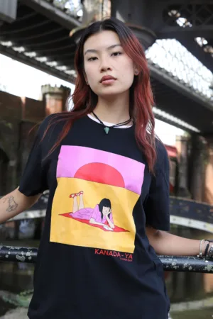 Kanada-Ya | Ramen Near Me | A person with long hair and tattoos stands under a bridge, wearing the Half Sun Front Print black T-shirt, showcasing a colorful design of someone lounging against a pink and orange sun background. | London