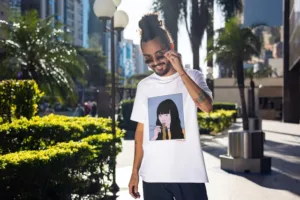 Kanada-Ya | Ramen Near Me | A person with long hair in a bun, wearing sunglasses and a white T-shirt named Noodle girl Ichi Front Print, stands on a sunny street lined with palm trees and buildings. | London